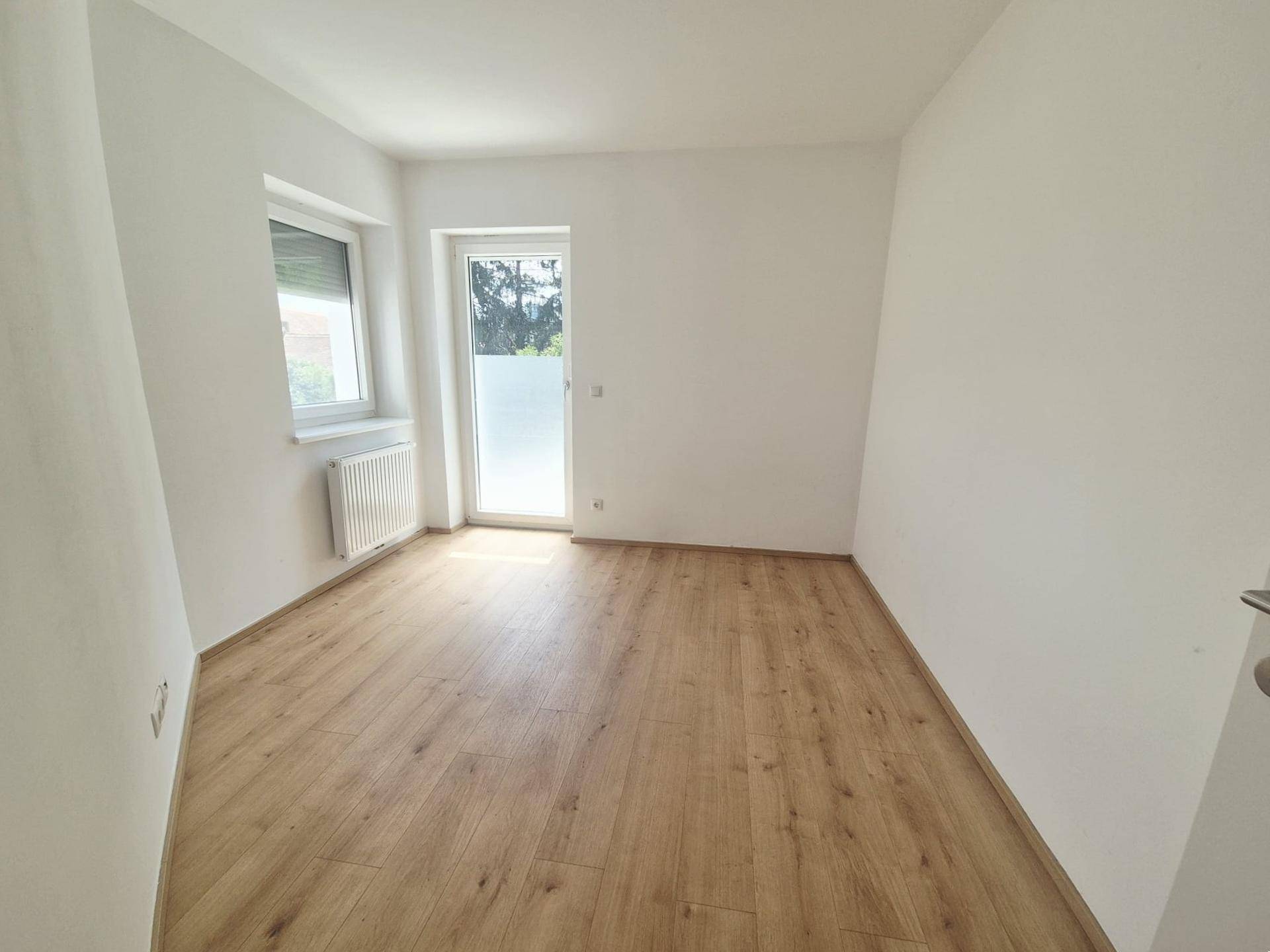 Helles Schlafzimmer mit modernem Laminatboden, weißen Wänden und Zugang nach draußen.