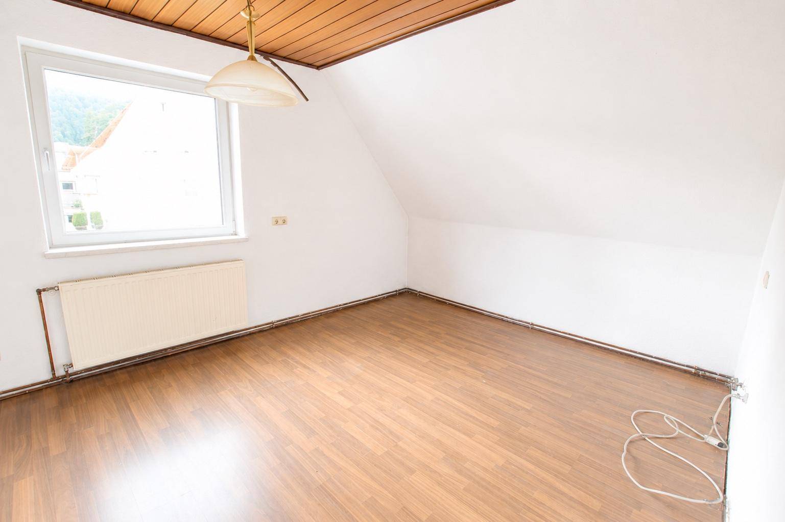 Helles Zimmer im Dachgeschoss mit Laminatboden, Holzdecke und Dachschräge, gut belichtet.