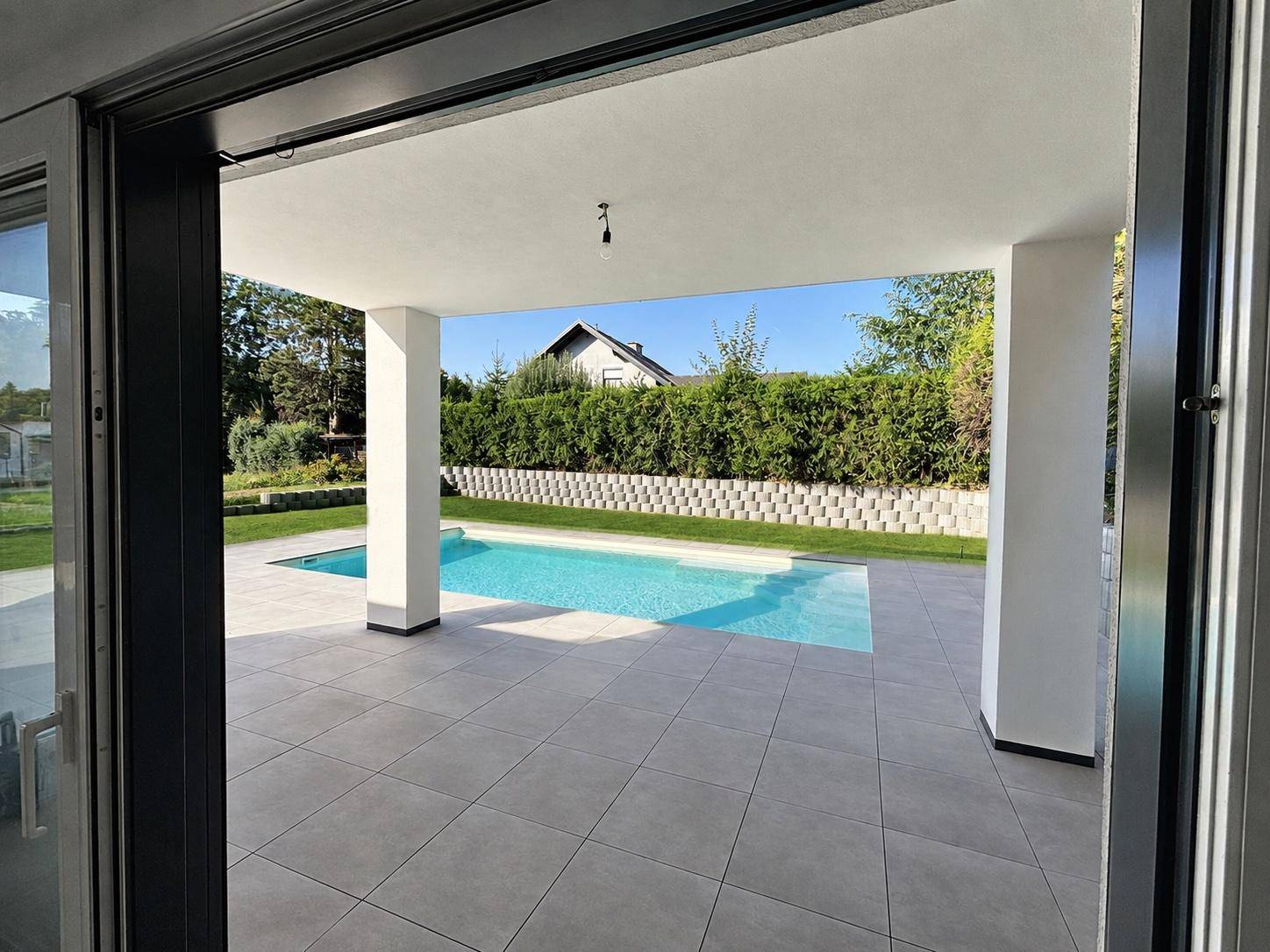 Blick von der überdachten Terrasse auf den Swimmingpool und den gepflegten Gartenbereich.