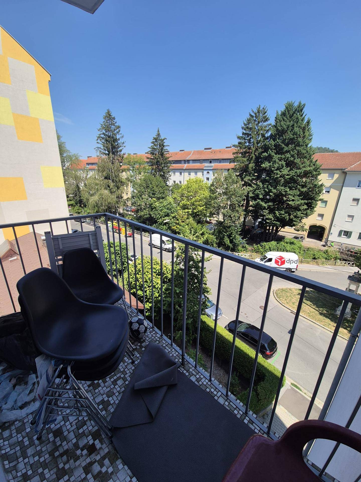 Balkon mit Sitzgelegenheiten und Ausblick auf die grüne Umgebung und Stadt.