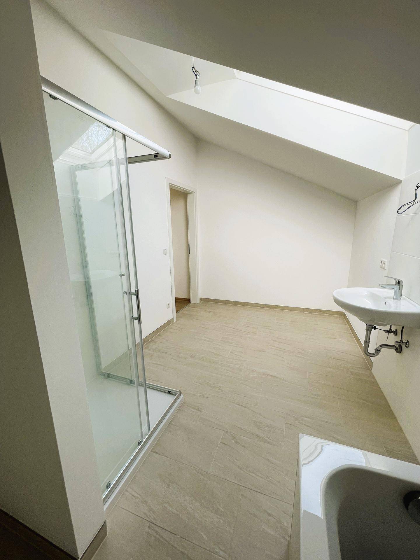 Geräumiges Badezimmer im Dachgeschoss mit Dusche, Waschbecken und Dachfenster für Tageslicht.