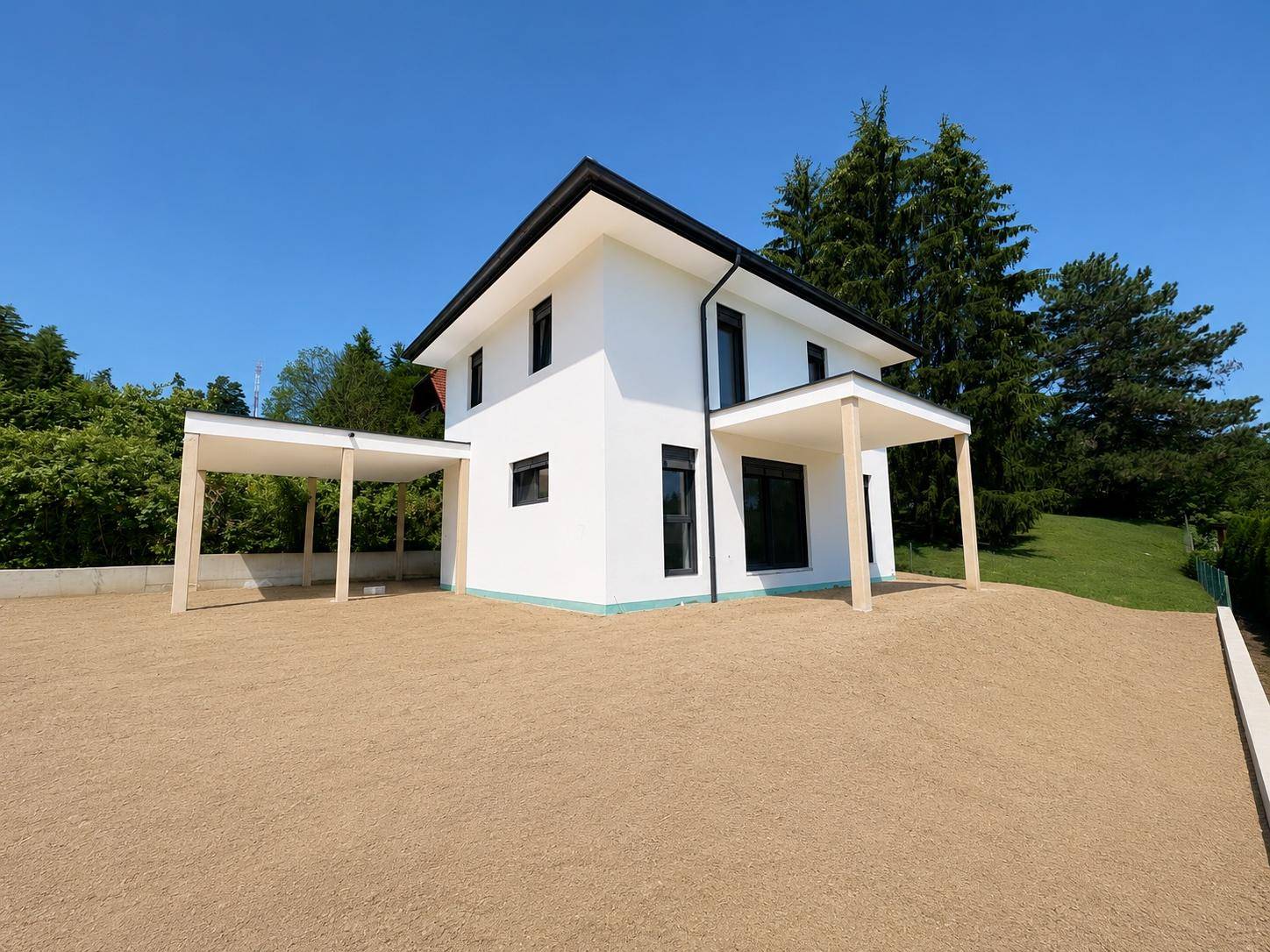 Modernes Einfamilienhaus mit weißer Fassade und Carport, umgeben von einer Kiesfläche.