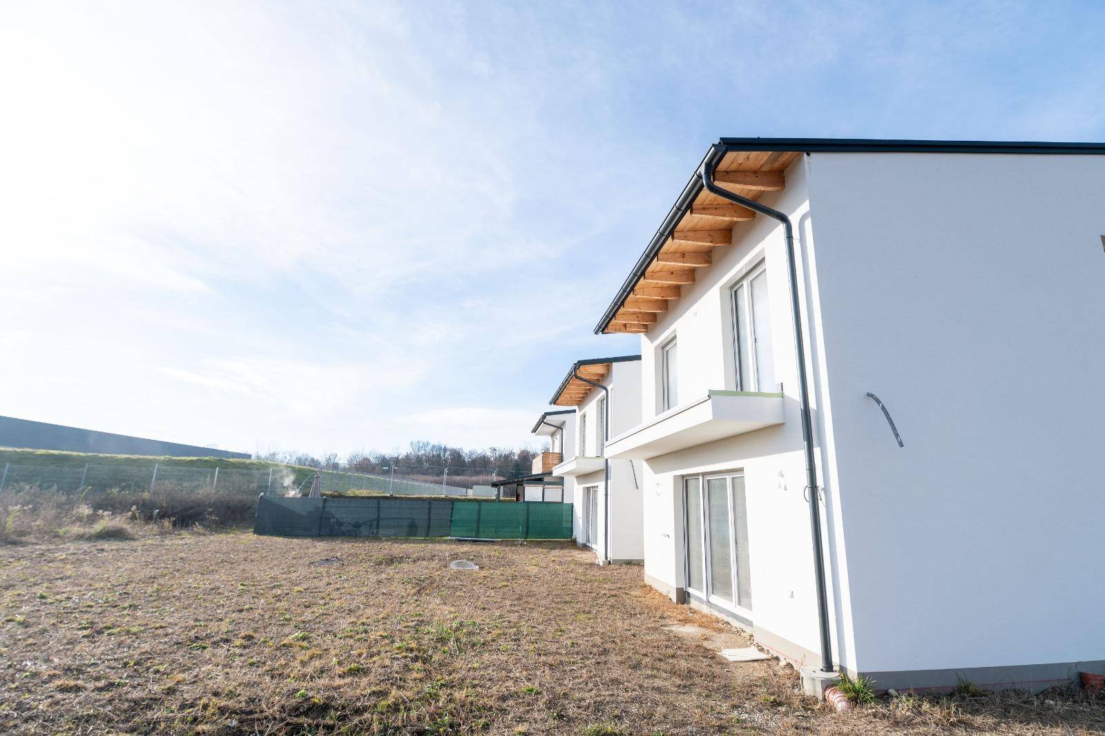 Seitenansicht der Neubauten mit sichtbaren Holzbalken unter dem Dach und weißer Fassade.
