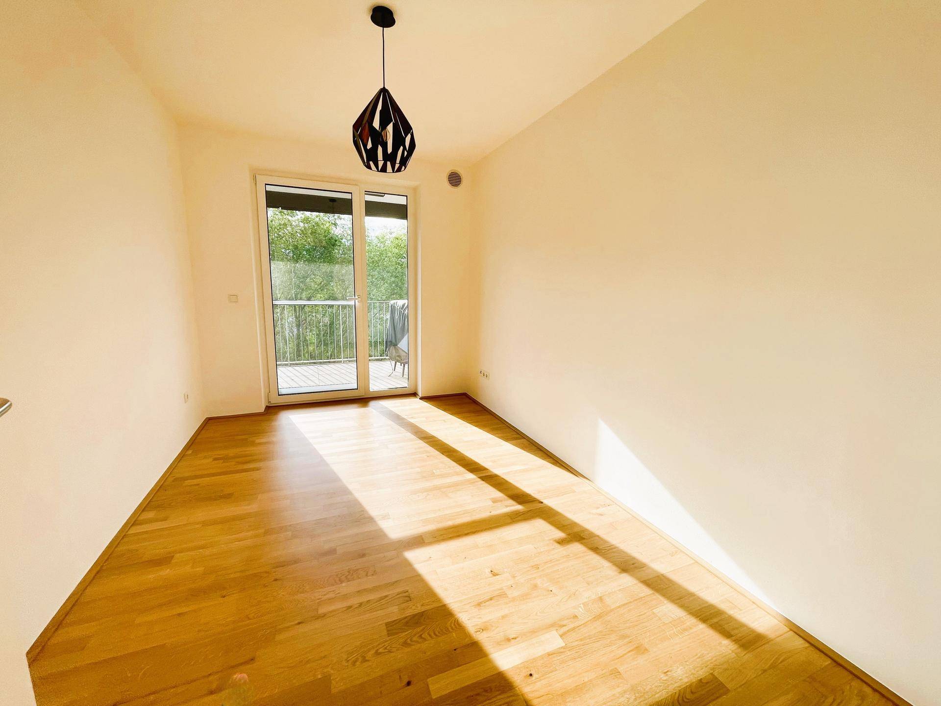 Helles, sonniges Zimmer mit Holzboden und großem Fenster mit Balkonzugang.