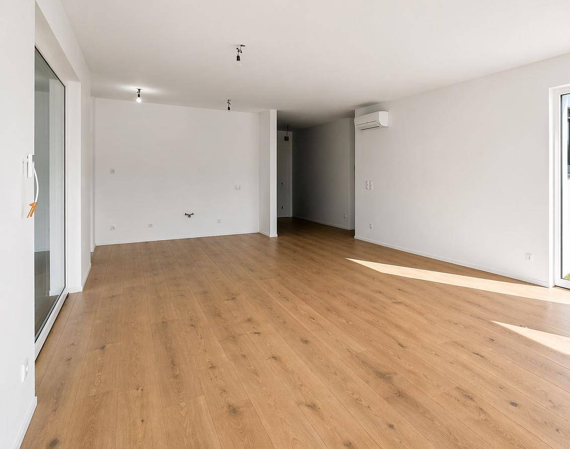 Geräumiger Wohnbereich mit Holzboden, Klimaanlage und viel Tageslicht durch große Fenster.
