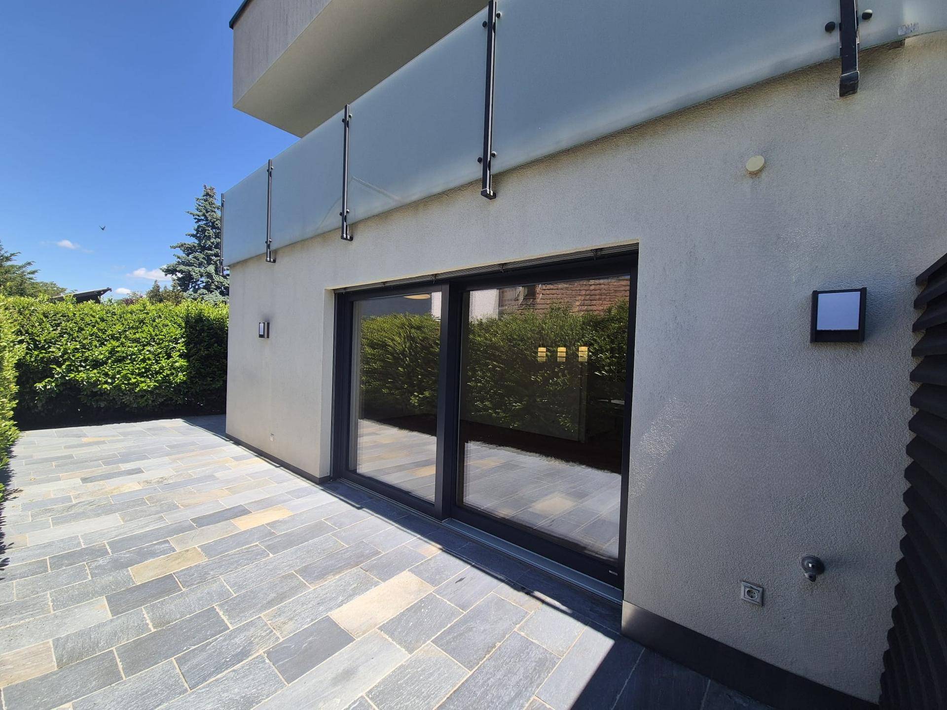 Sonniger Terrassenbereich mit Steinplatten und Hecke, ideal für entspannte Stunden im Freien.