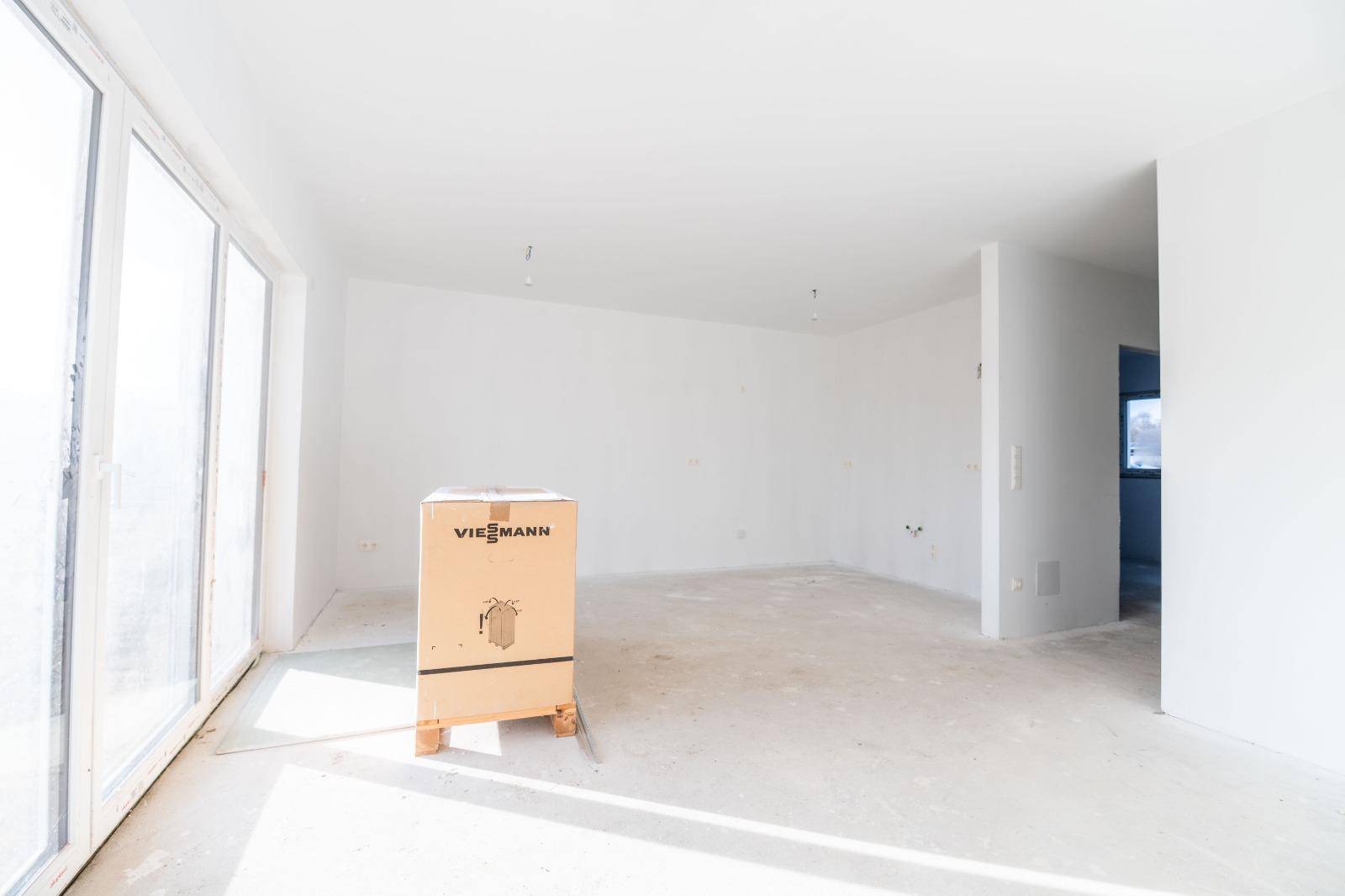 Lichtdurchfluteter Wohnbereich im Rohbau mit großen Fenstern und einer Viessmann-Verpackung.