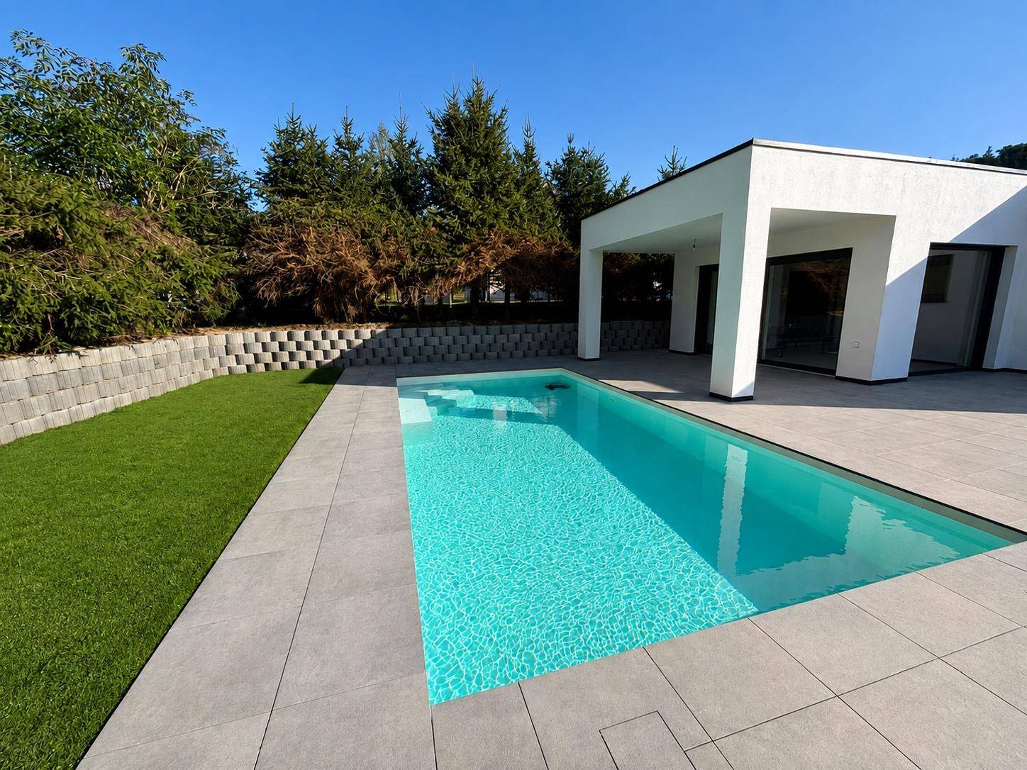 Langer, rechteckiger Swimmingpool mit hellen Fliesen umgeben von einer modernen Terrasse.