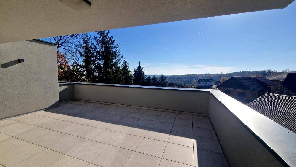 Geräumige Terrasse mit hellen Fliesen und weitem Blick über die umliegende Landschaft und Dächer.