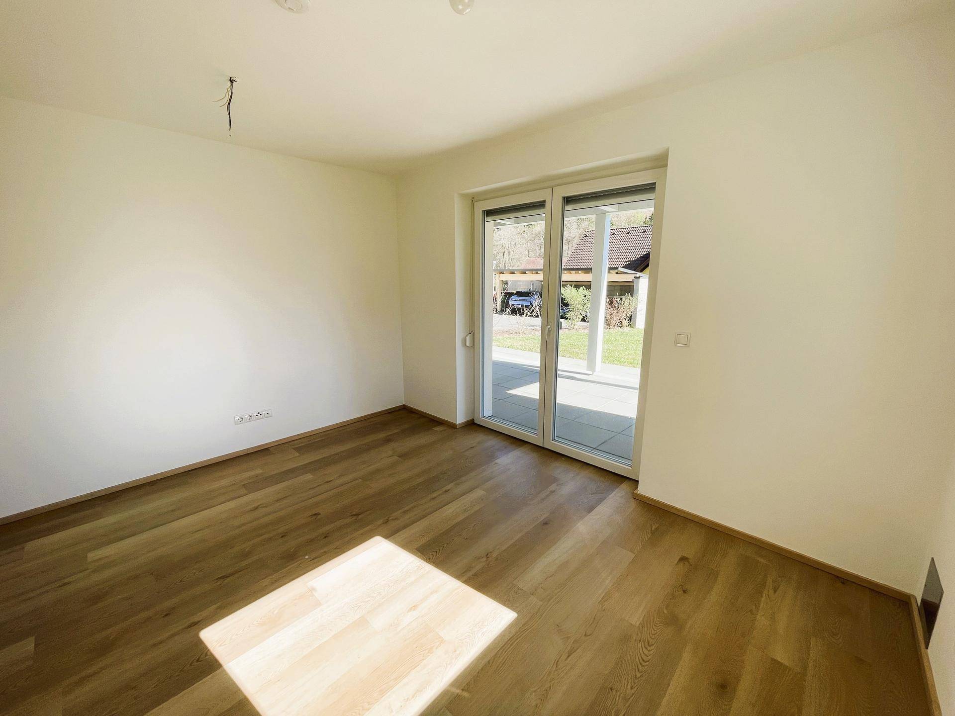 Helles Zimmer mit Holzfußboden und großen Schiebetüren, die viel Tageslicht hereinlassen.