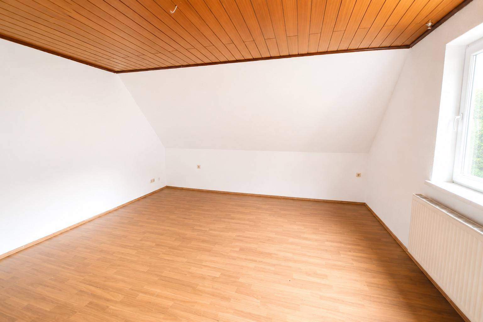 Geräumiges Dachzimmer mit Laminatboden, Holzdecke und schrägen Wänden, bietet viel Platz.