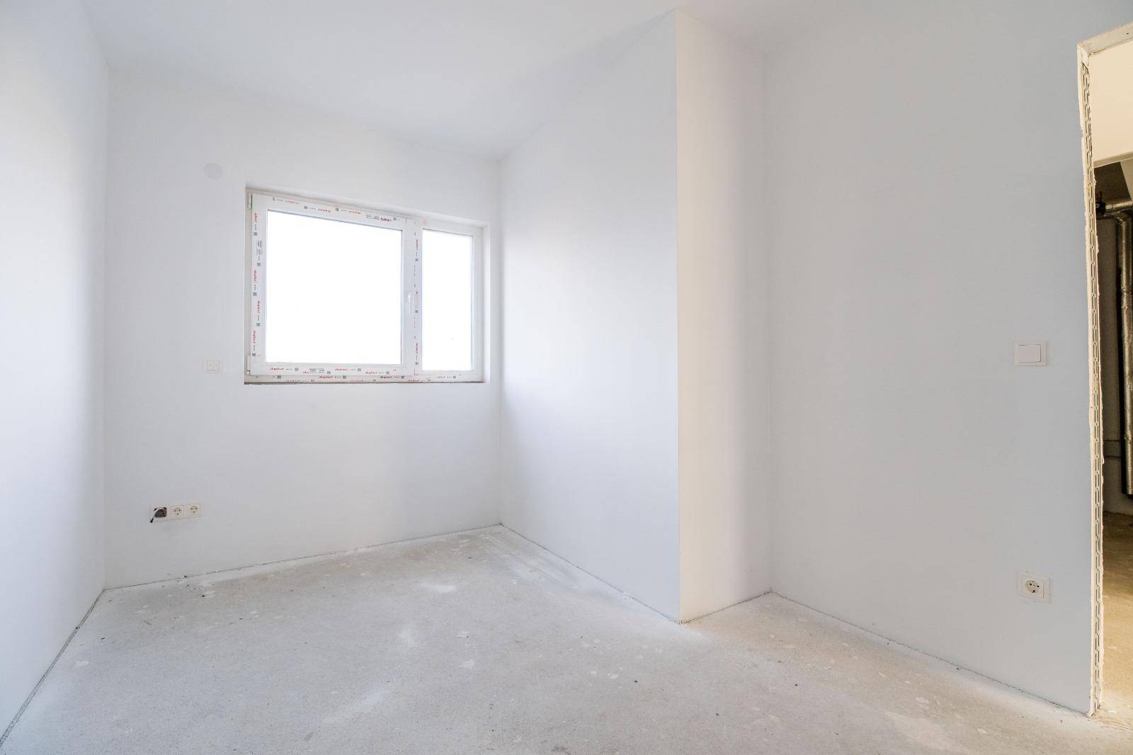 Schlafzimmer im Rohbau mit weiß gestrichenen Wänden und einem Fenster.