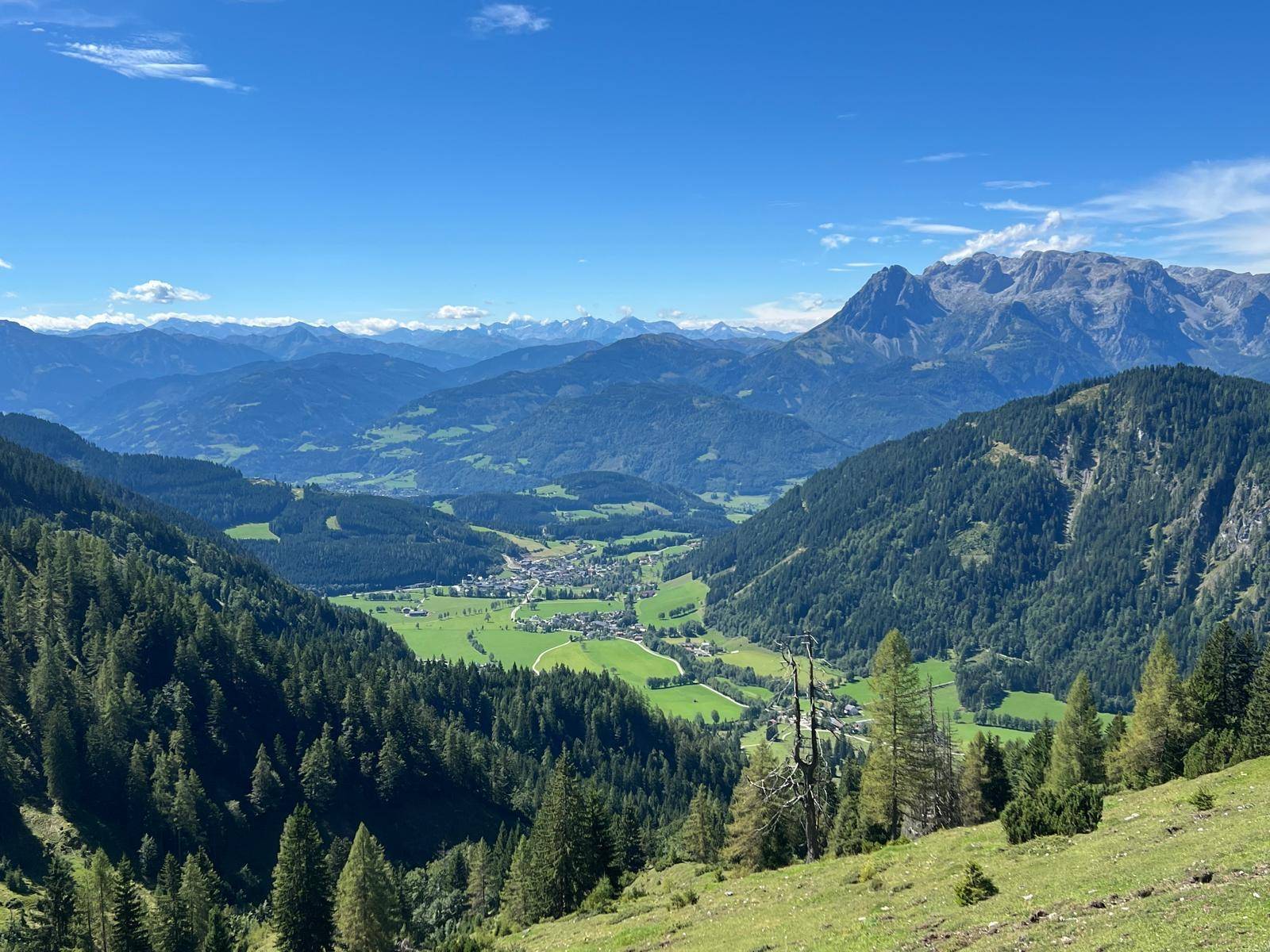 Atemberaubender Panoramablick über ein grünes Tal mit einem Dorf, umgeben von Wäldern und Bergen.