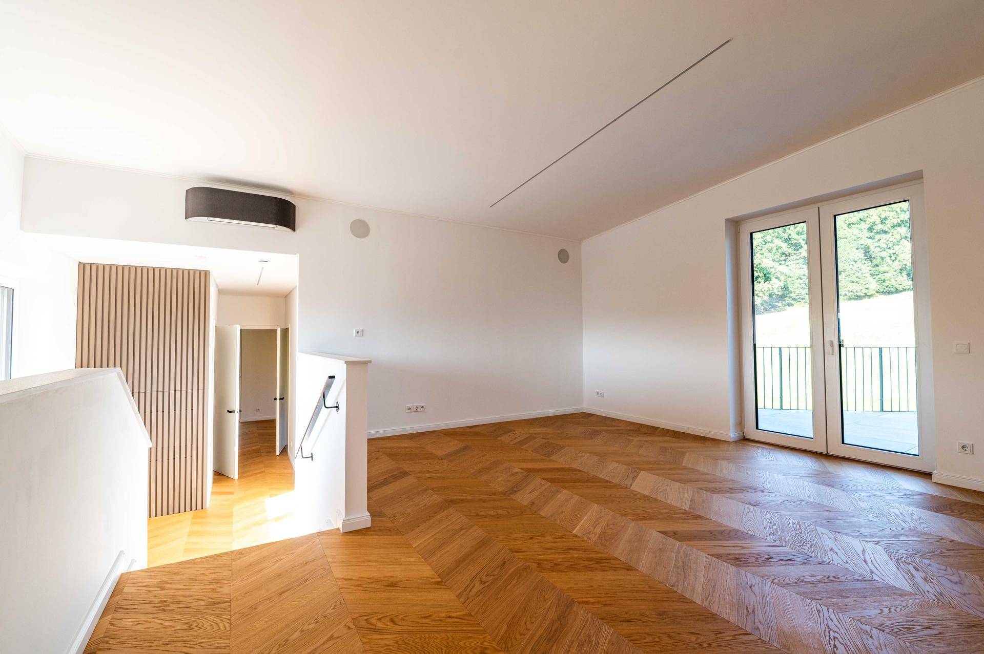Offener Wohnbereich im Obergeschoss mit Fischgrätparkett und Zugang zur Terrasse.