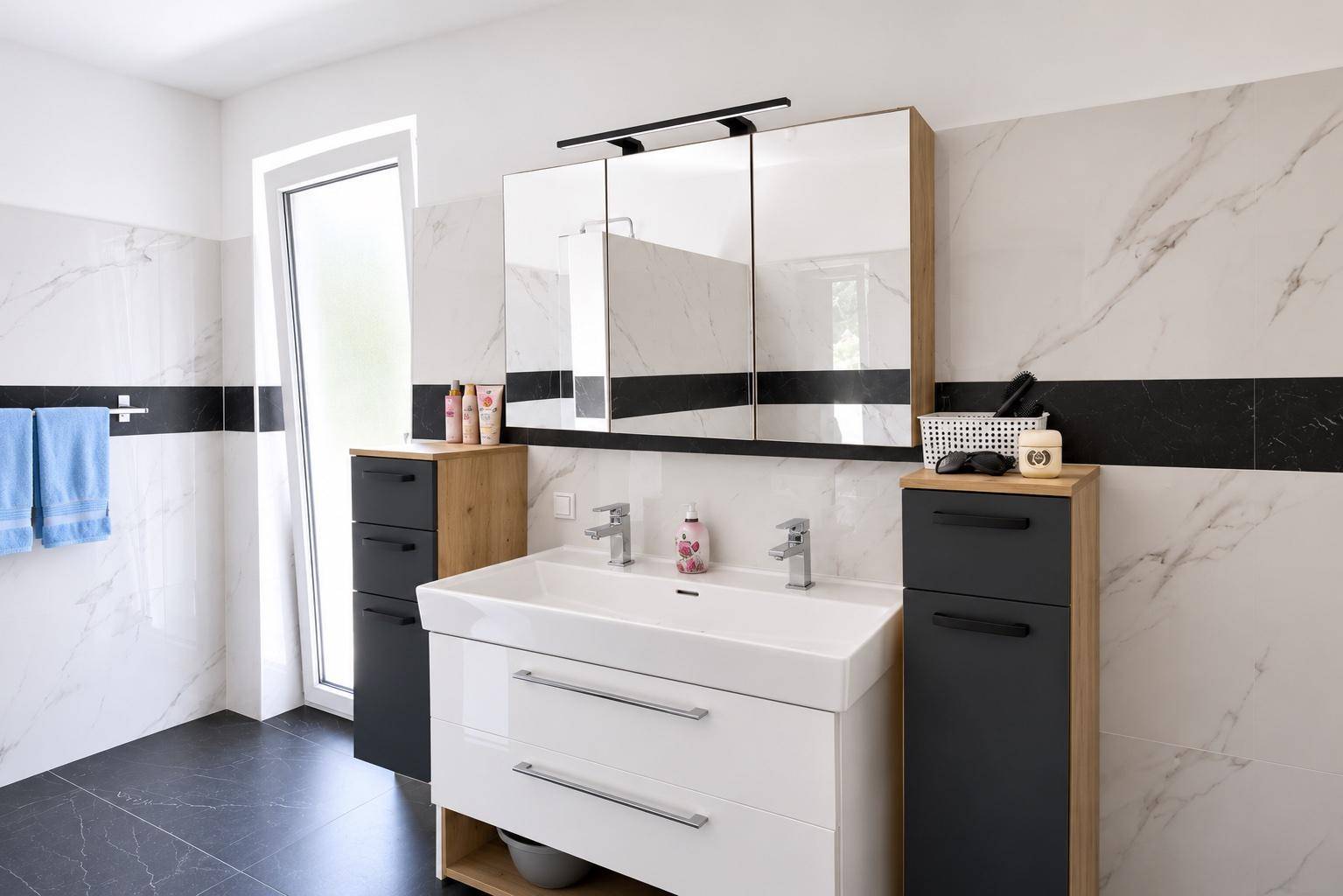 Helles Badezimmer mit Doppelwaschbecken, Spiegelschrank und Fenster.