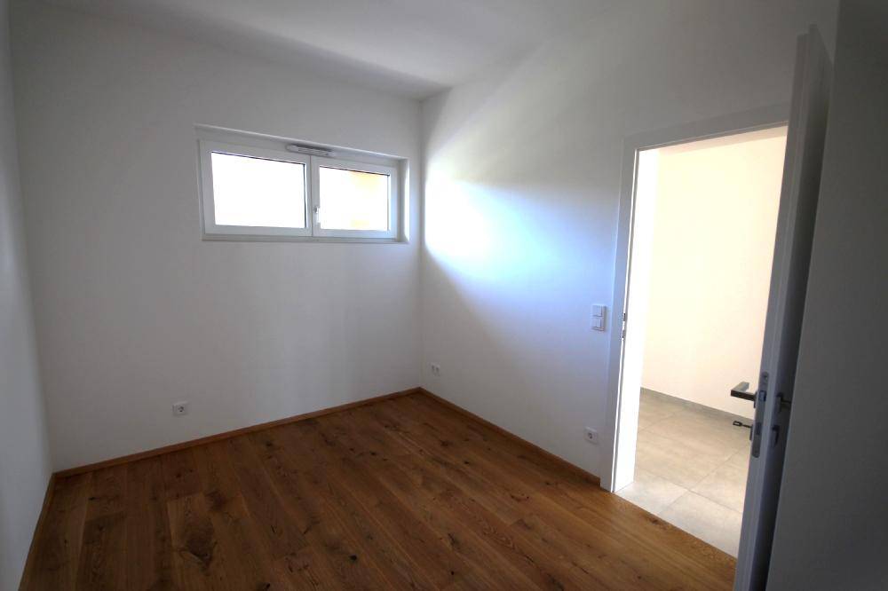 Helles Schlafzimmer mit Holzboden und Fenster, bereit zur individuellen Gestaltung.
