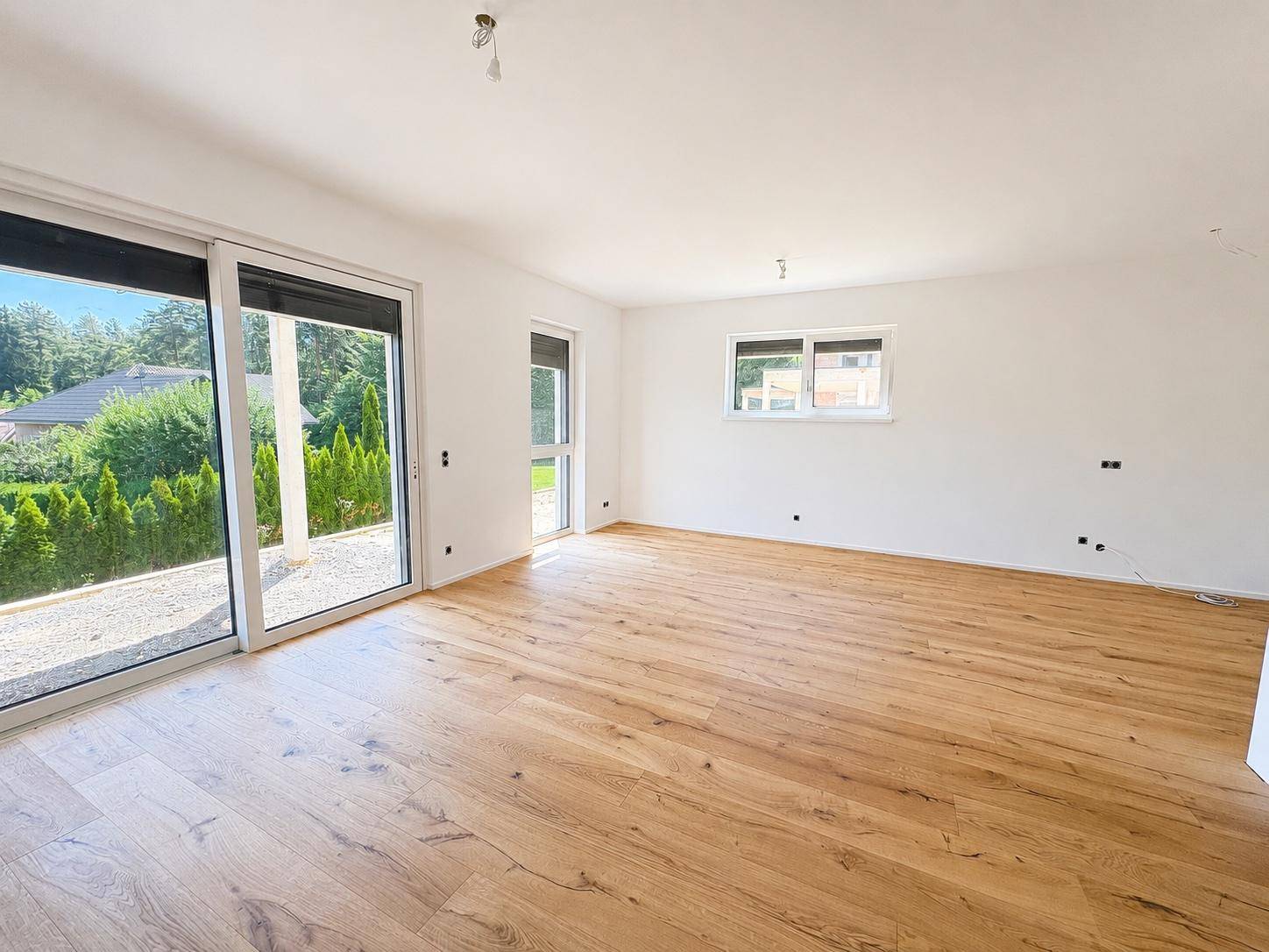 Geräumiges Wohnzimmer mit Holzboden, weißen Wänden und großen Schiebetüren zum Außenbereich.