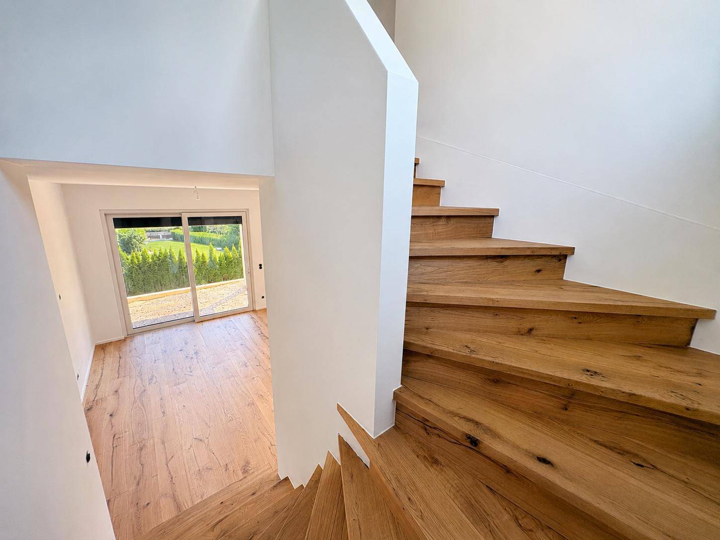 Moderne Holztreppe führt in das Obergeschoss, mit Blick auf einen hellen Raum im Erdgeschoss.