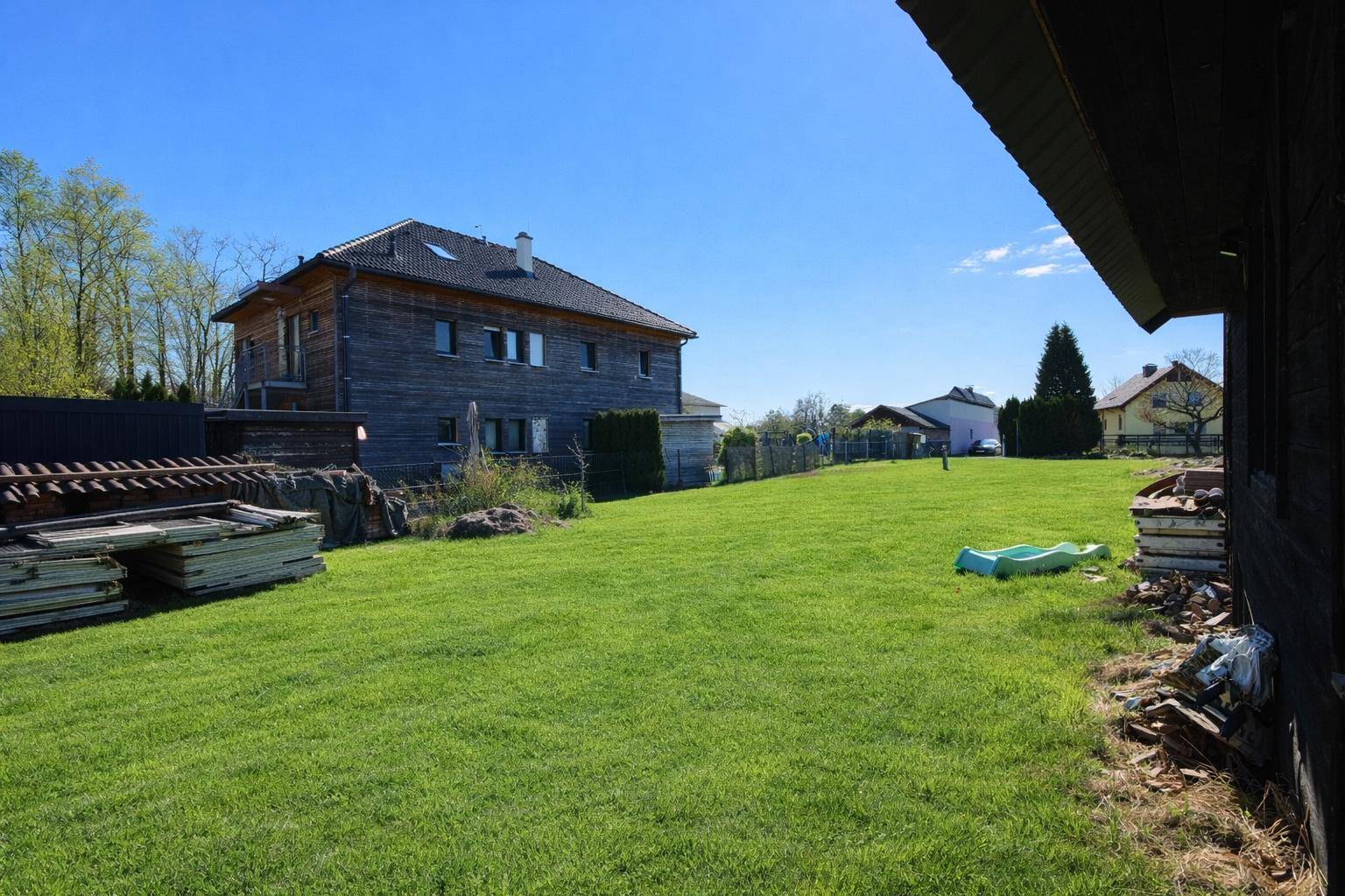 Sonniges Grundstück mit großem Rasenbereich und einem Holzhaus in ländlicher Umgebung.