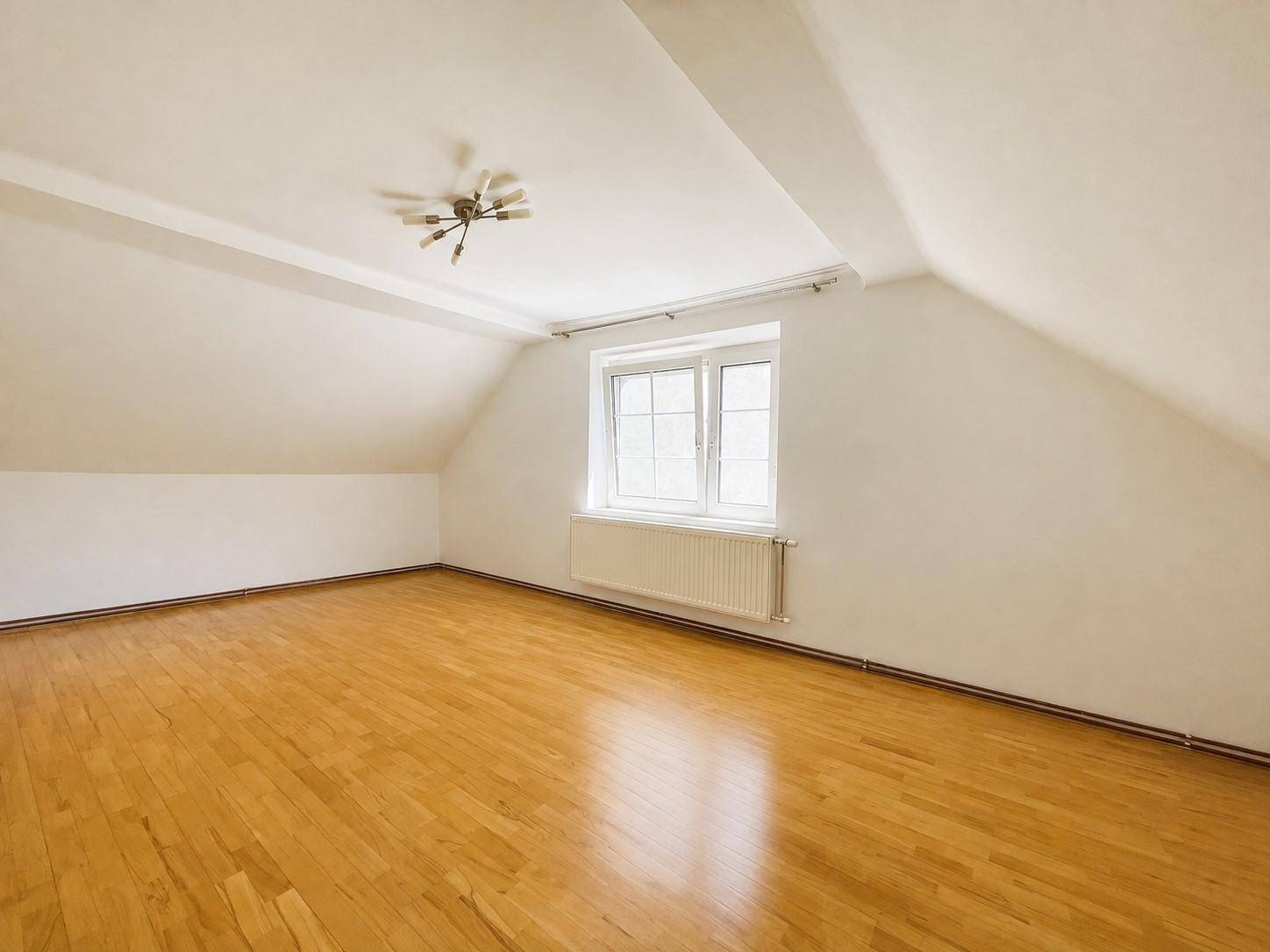 Geräumiger Dachgeschossraum mit hellem Holzfußboden und einem großen Fenster.