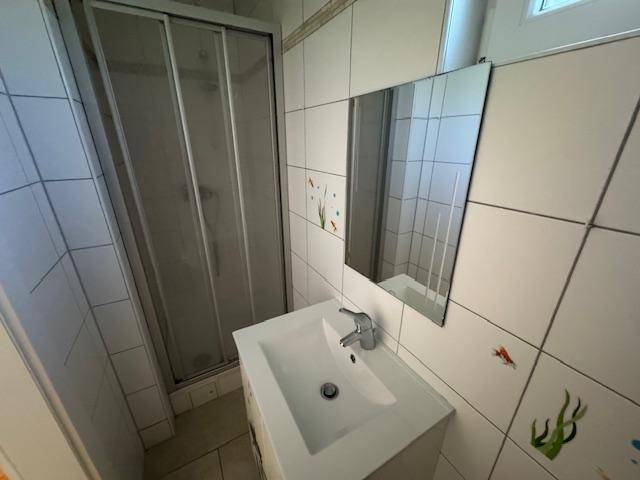 Badezimmer mit Duschkabine, Waschbecken und Spiegel, hell gefliest mit Fischmotiven.