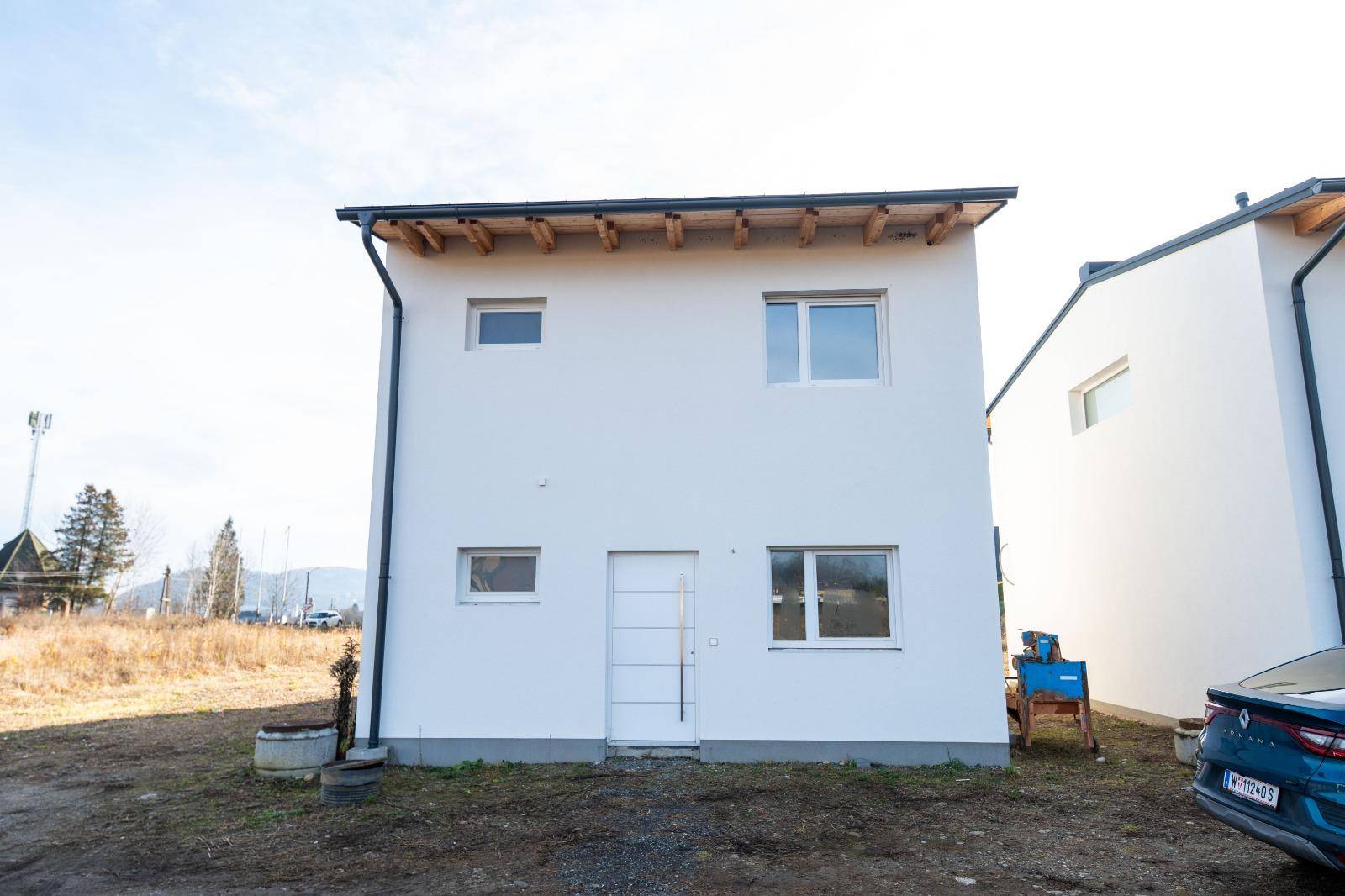 Vorderansicht eines modernen Neubaus mit weißer Fassade, Eingangstür und großen Fenstern.