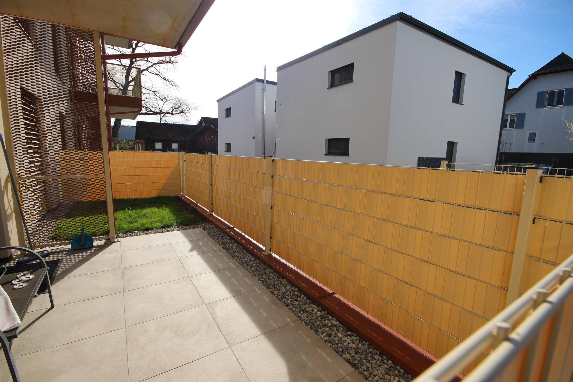 Private Terrasse mit Fliesenboden, Sichtschutz und kleinem Rasenbereich.