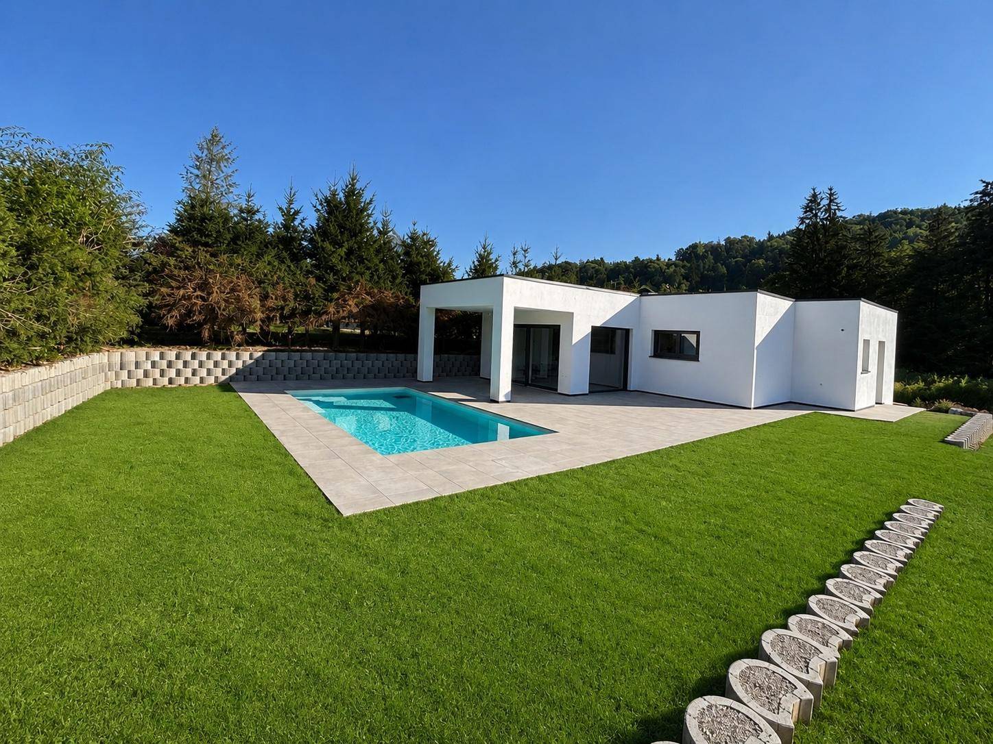 Neubau-Bungalow mit klarem Design, umgeben von Grünflächen und einem erfrischenden Pool.
