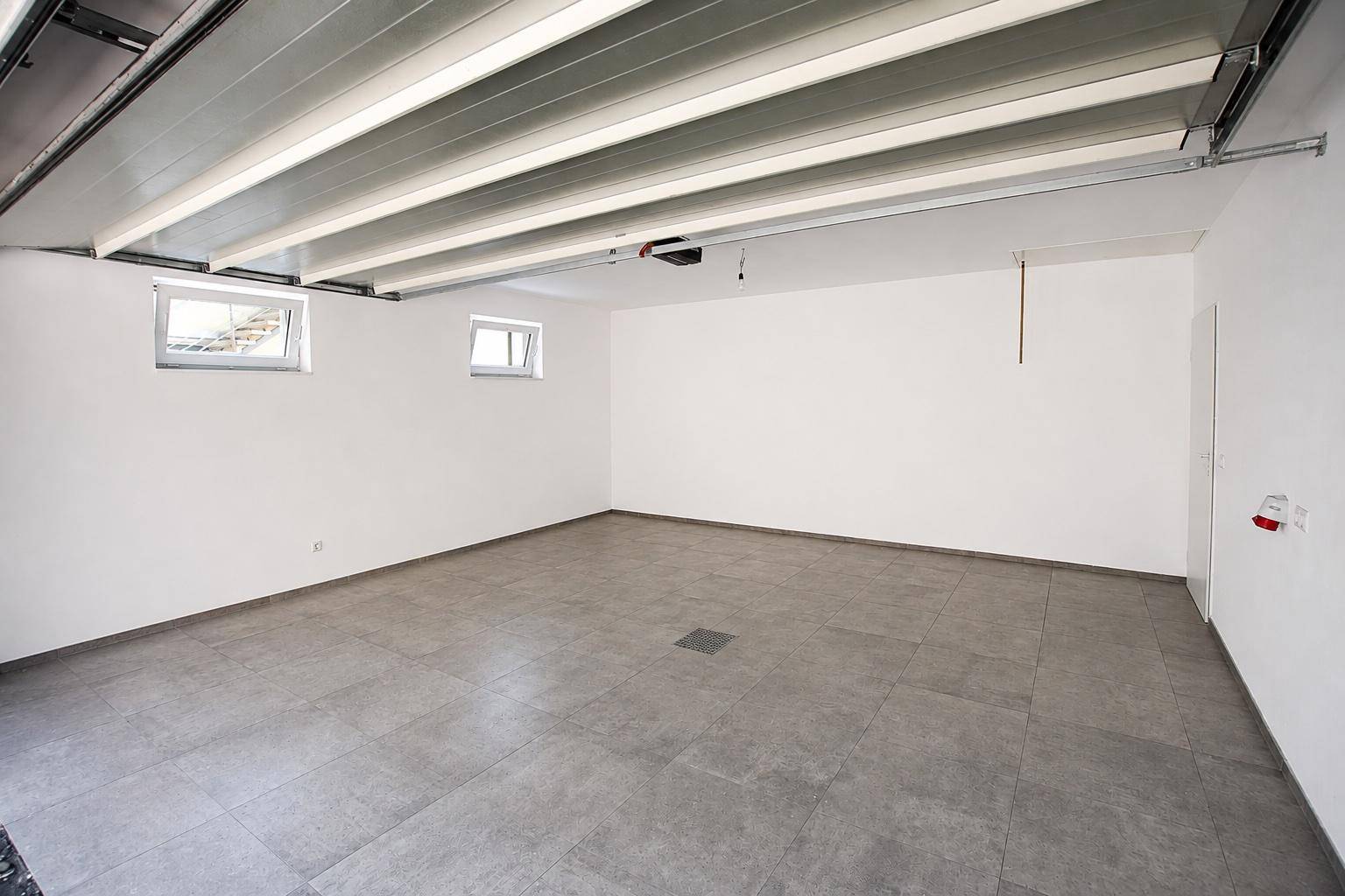Geräumige Garage mit Fliesenboden und Fenstern für Tageslicht.
