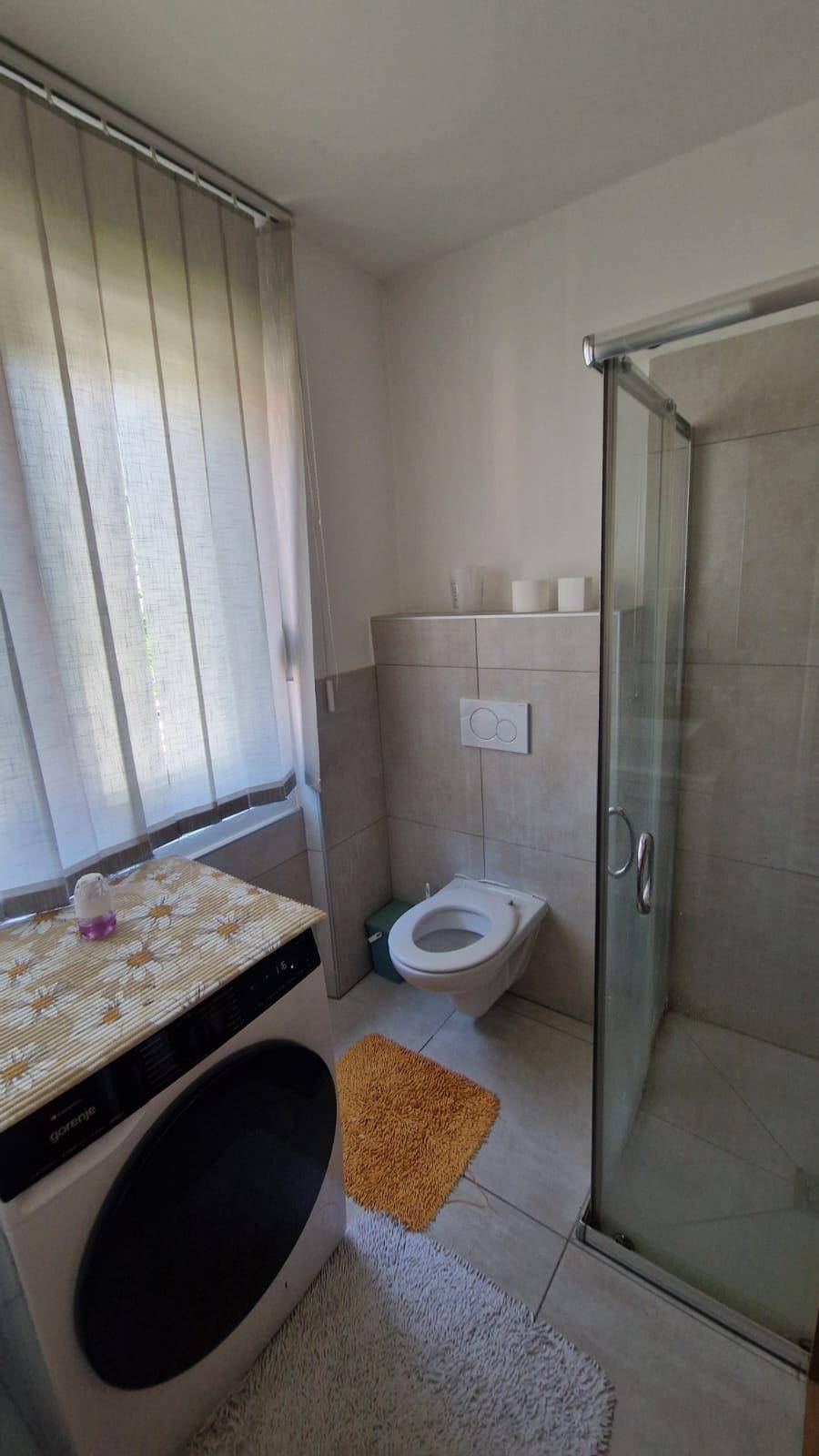 Funktionales Badezimmer mit Duschkabine, Toilette und Waschmaschine, hell gefliest.