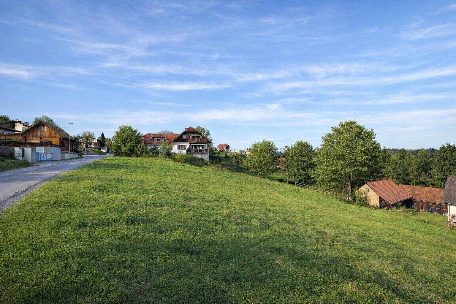 Grüne Hügellandschaft mit einer Straße und Wohnhäusern im Hintergrund unter klarem Himmel.