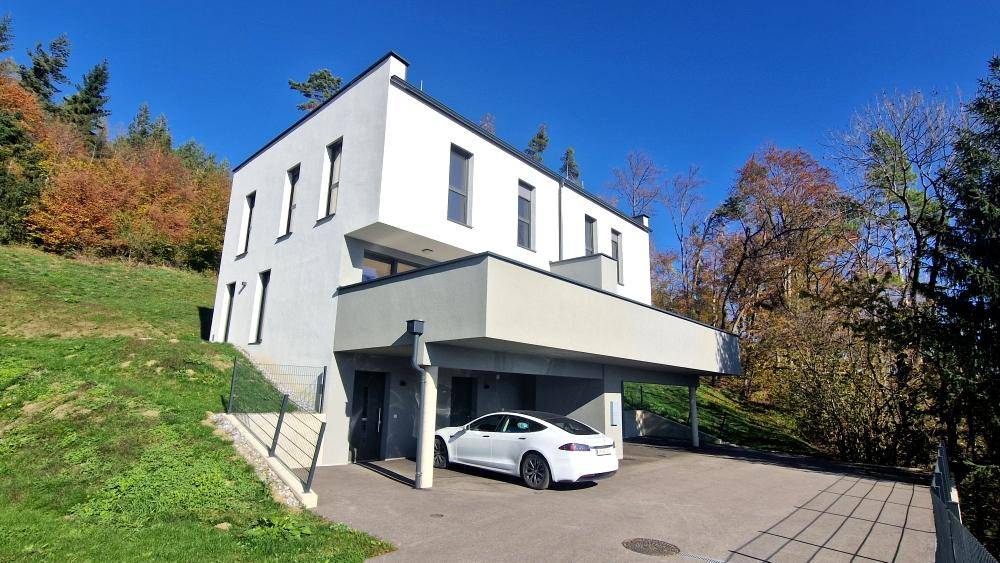 Modernes Wohnhaus mit Carport und umgebender Natur unter blauem Himmel.