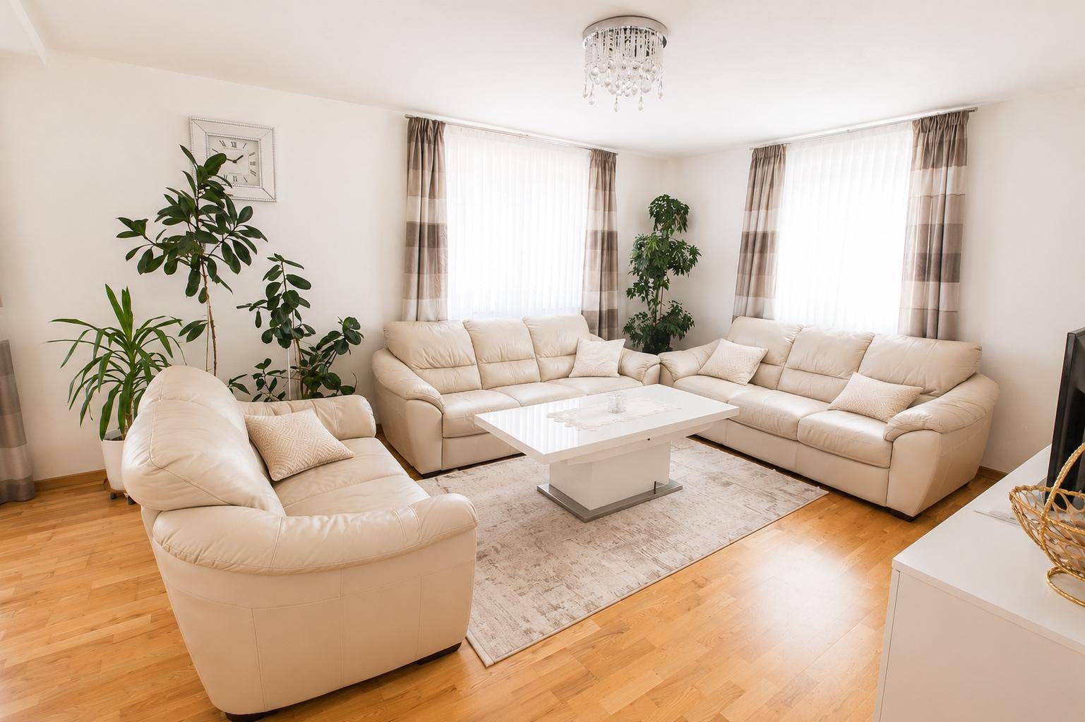 Helles Wohnzimmer mit beigen Ledersofas, Holzboden und Kronleuchter.