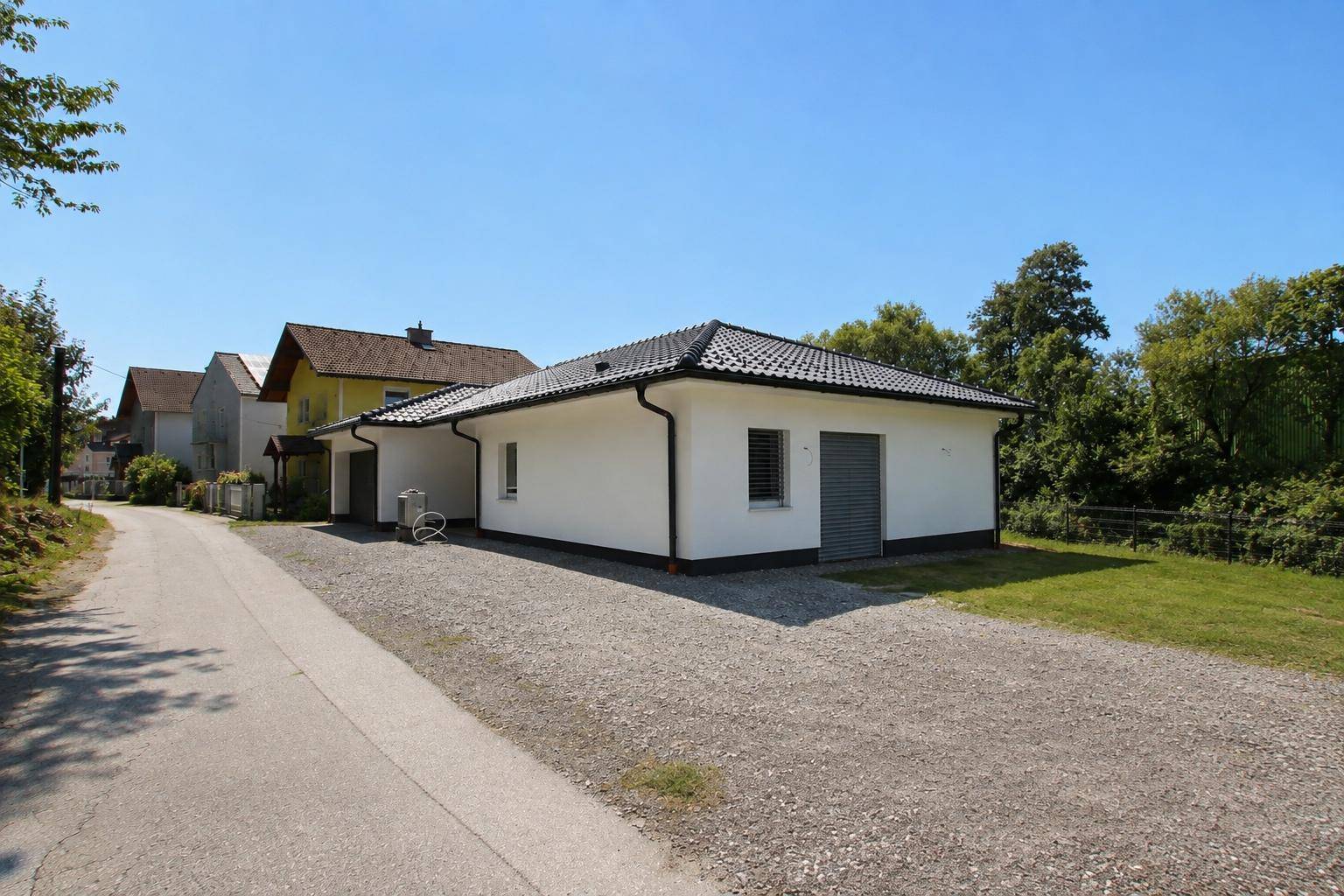 Ansicht des Bungalows von der Zufahrt mit Schotterparkplatz und angrenzenden Häusern.