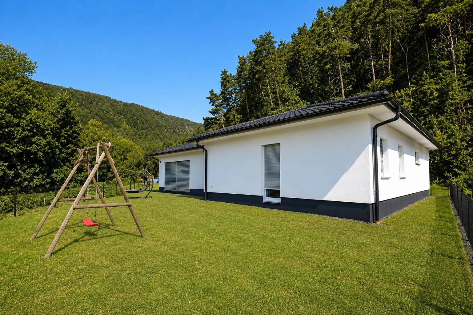 Moderner Bungalow mit weißer Fassade und großem Garten in ruhiger, grüner Umgebung.