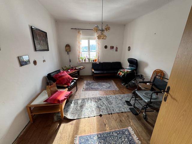 Wohnzimmer mit Holzfußboden, Sofa, Sesseln und einem Fenster, das viel Tageslicht hereinlässt.