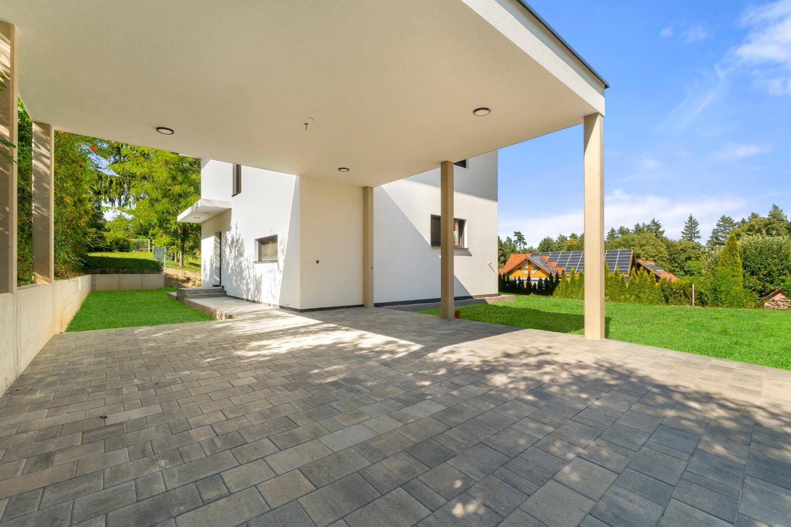 Geräumiger Carport mit gepflastertem Boden und Blick auf die grüne Umgebung.