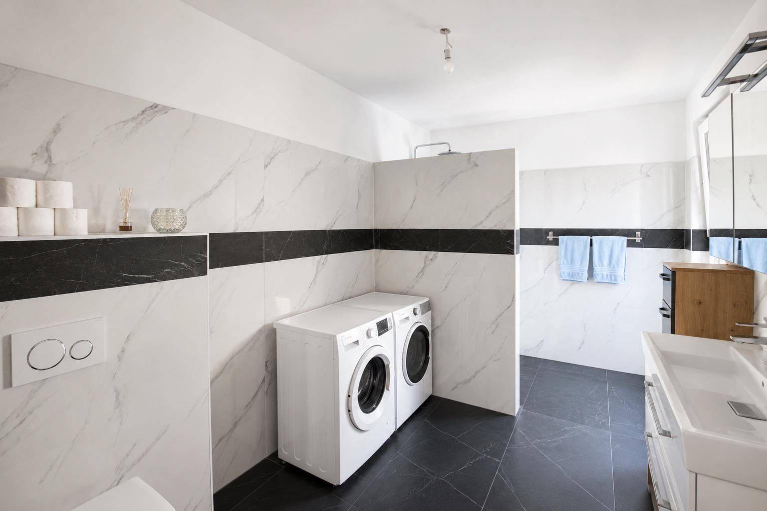 Modernes Badezimmer mit Waschmaschine, Trockner und eleganten Marmorfliesen.