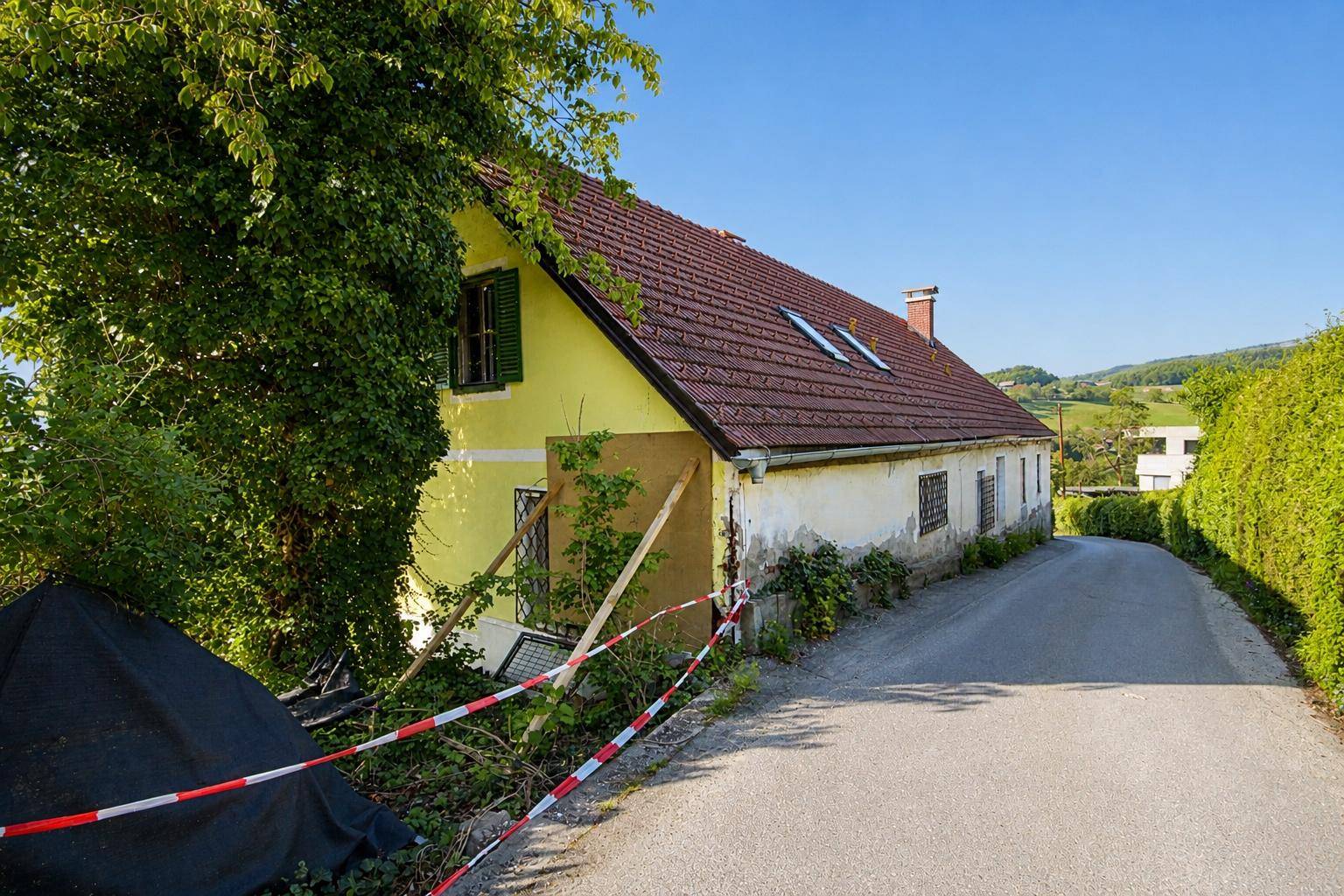 Älteres Haus mit gelber Fassade, rotem Dach und Absperrband an der Seite.