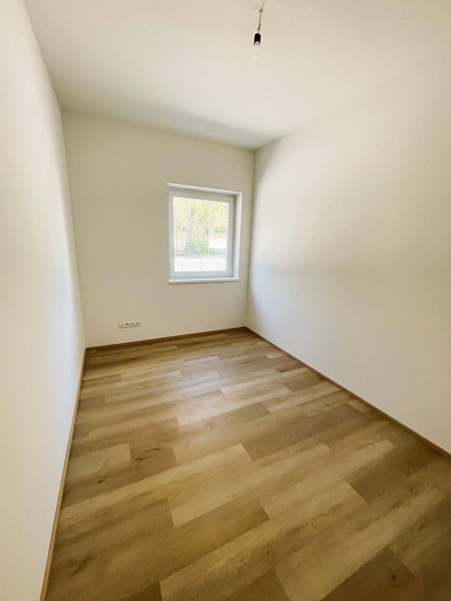 Helles Zimmer mit modernem Laminatboden und einem Fenster, ideal als Schlaf- oder Arbeitszimmer.