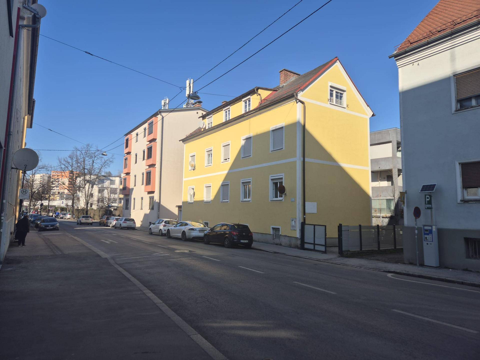 Ansicht des gelben Gebäudes von der Straße aus mit umliegenden Häusern und blauem Himmel.