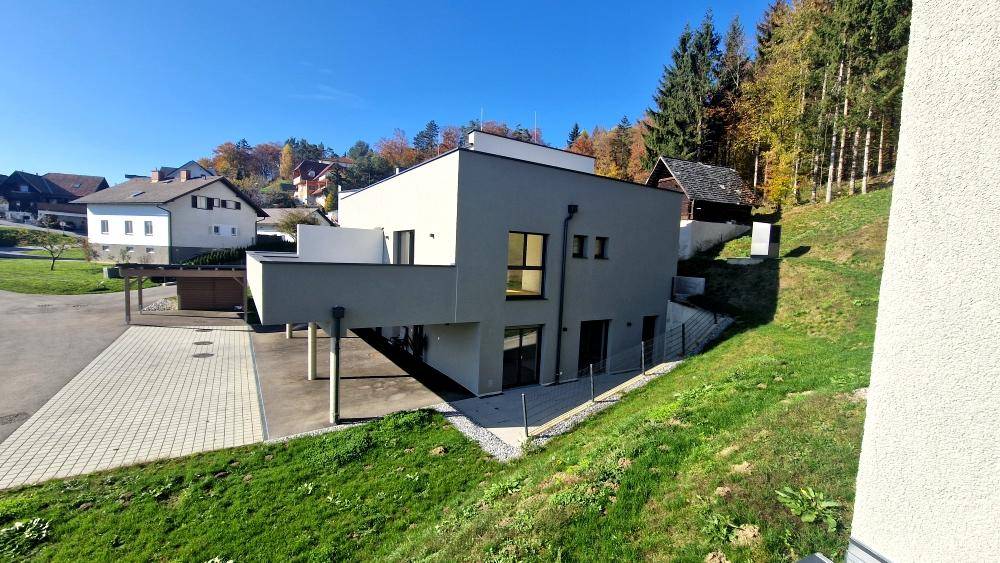 Zeitgenössisches Gebäude mit klarer Architektur, umgeben von einer hügeligen Grünfläche und Bäumen.