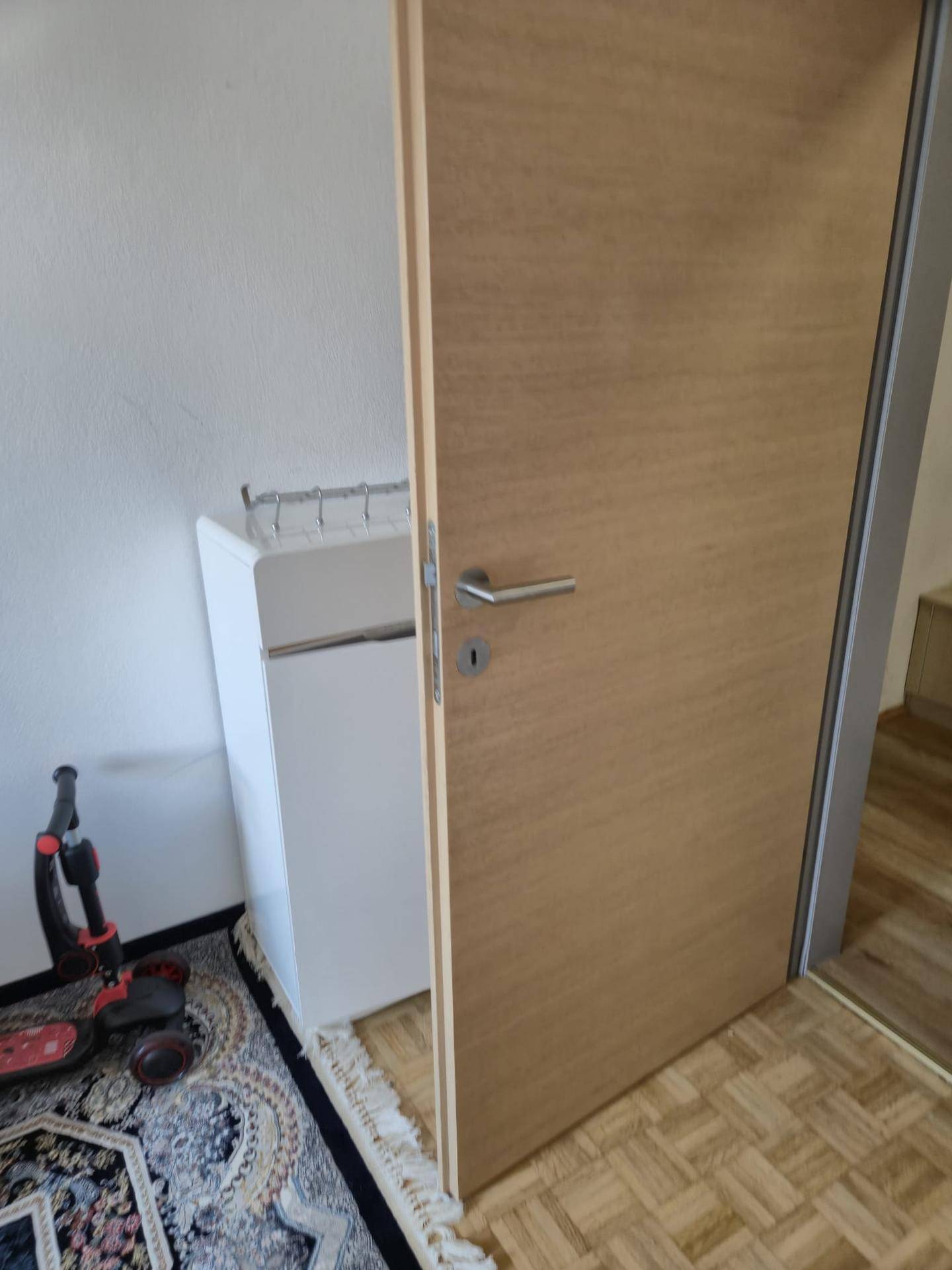 Holztür und ein kleiner weißer Schrank in einem Innenraum mit Teppichboden.
