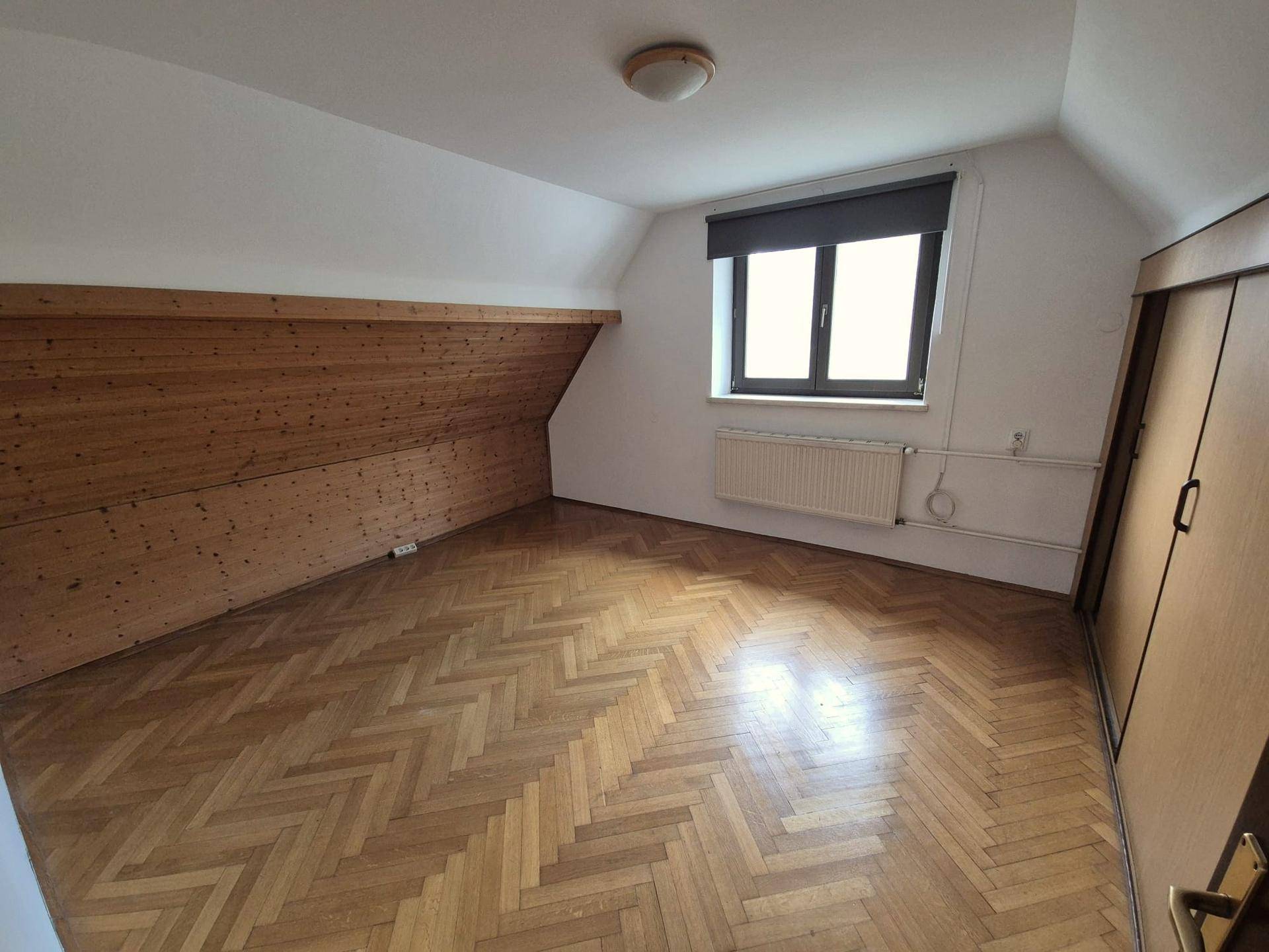 Gemütliches Schlafzimmer mit Dachschräge, Fischgrätparkett und einem Fenster.