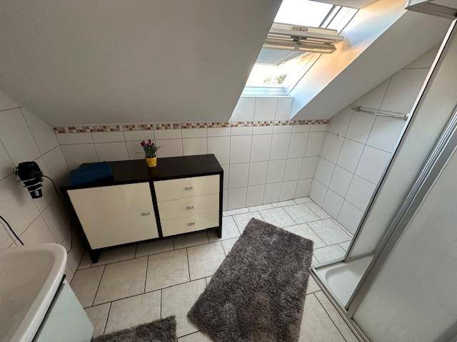 Helles Badezimmer im Dachgeschoss mit Duschkabine, Dachfenster und weißen Fliesen.