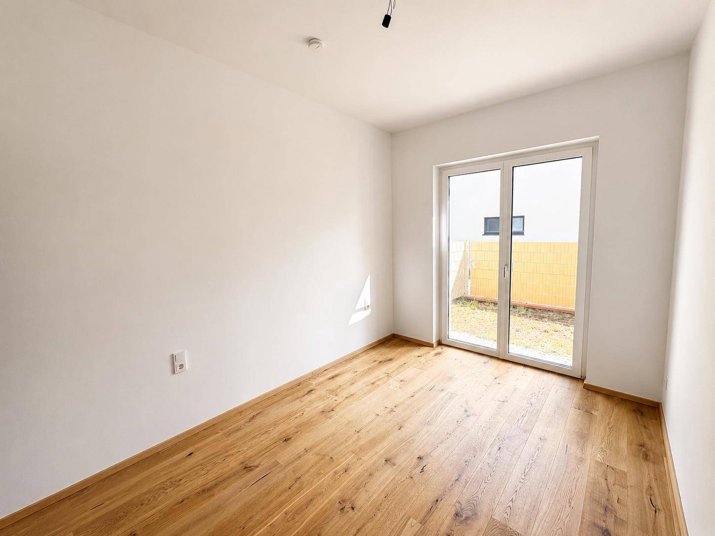 Helles Schlafzimmer mit Holzboden und direktem Zugang zu einem kleinen Gartenbereich.