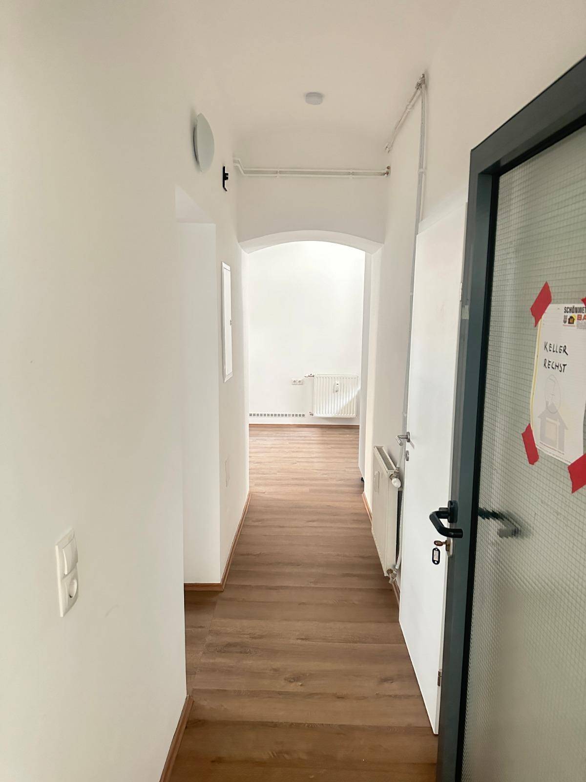 Langer, heller Flur mit Laminatboden, der zu einem weiteren Zimmer führt.