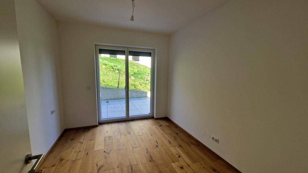 Schlafzimmer mit Holzboden und Schiebetür, die zu einem Außenbereich mit Grünblick führt.