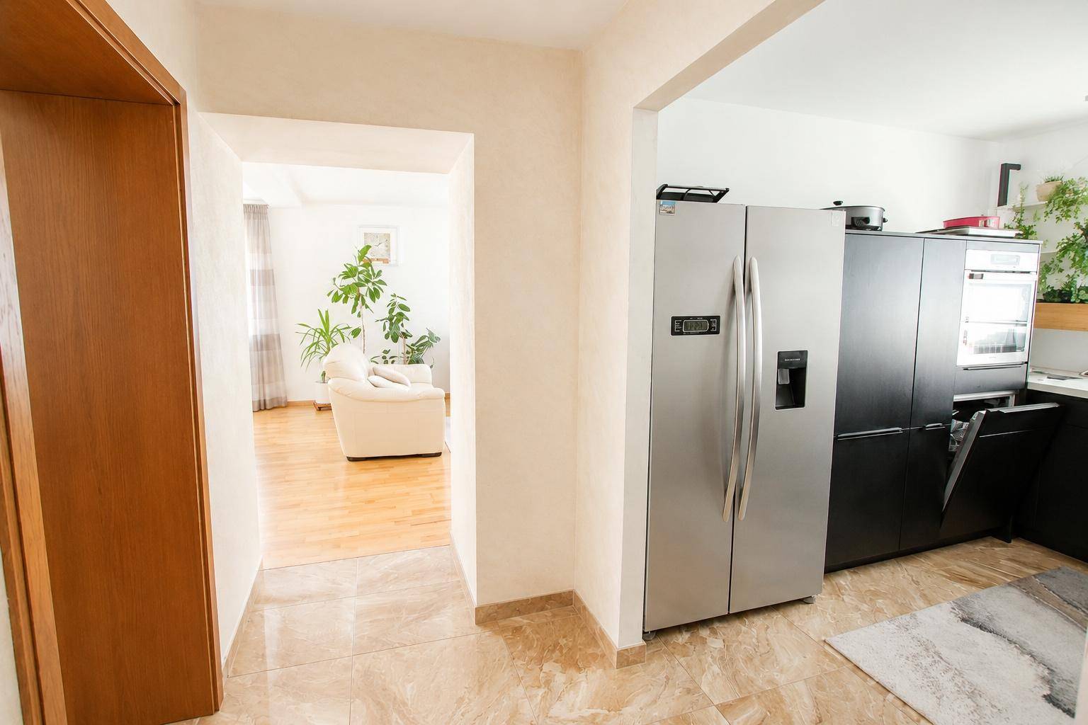 Übergang vom Flur zur modernen Küche mit großem Kühlschrank und Blick ins Wohnzimmer.