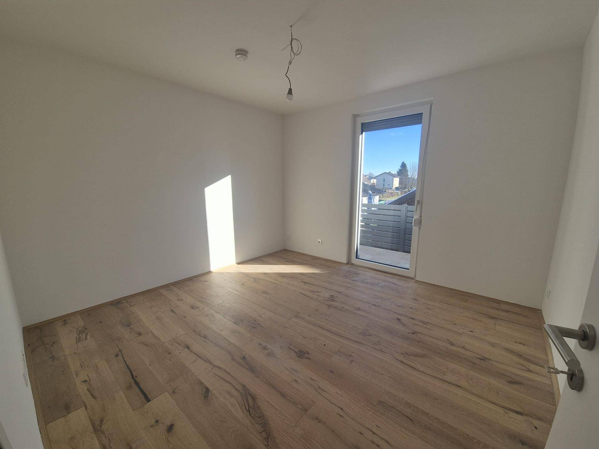 Helles Zimmer mit neuem Holzboden und Zugang zu einem Balkon, ideal als Schlafzimmer.